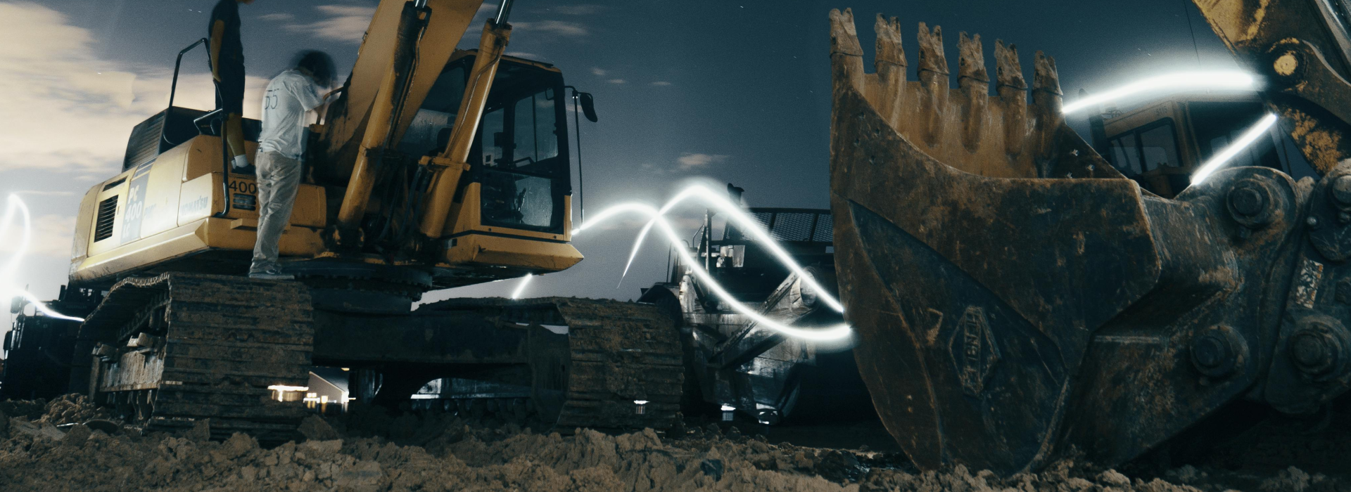 A powerful excavator at a construction site under the night sky, with workers around.