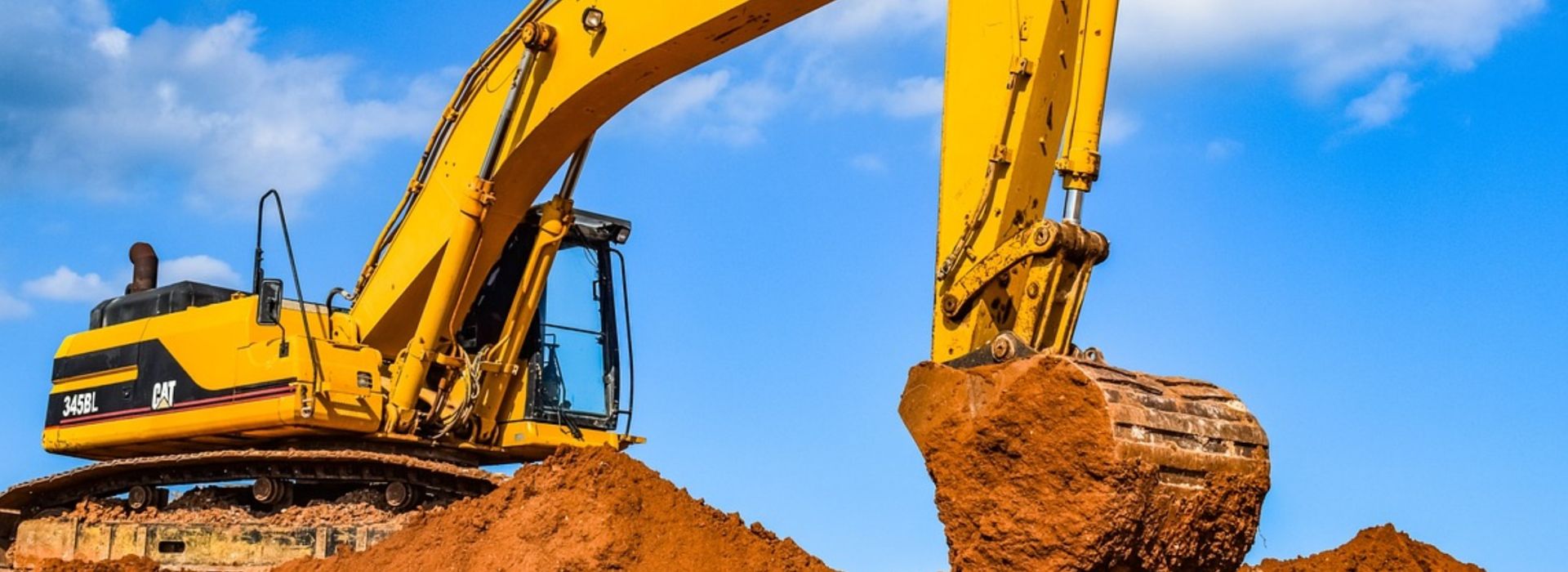 An orange bulldozer at work, moving sand under a clear blue sky on a construction site.